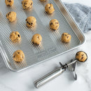 Baking tray with cookie dough balls and a cookie scoop on a marble surface