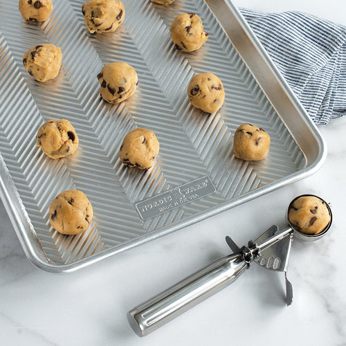 Baking tray with cookie dough balls and a cookie scoop on a marble surface