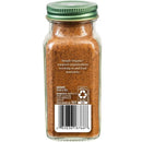 A glass spice jar filled with nutmeg, featuring a green metal lid and a white paper label with a barcode and product text, shown against a plain white background.