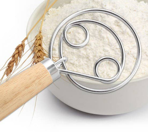 Metal dough whisk with wood handle in a bowl of flour on a white background