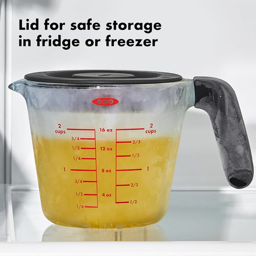 A glass measuring cup with a lid holding yellow liquid in a freezer with frost on it and text noting that the lid is safe for the fridge or freezer.