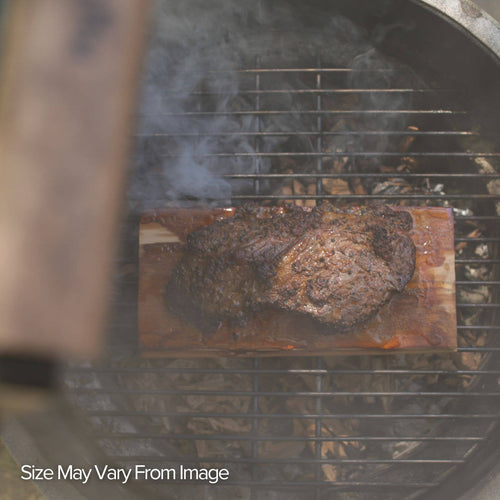 Roast on a wooden grilling plank placed on a hot grill with smoke rising, close-up view.