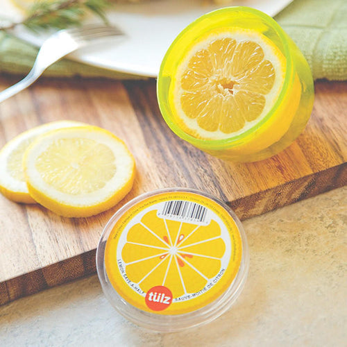 A lemon in a lemon saver with the lid next to it with lemon slices on a wooden cutting board.