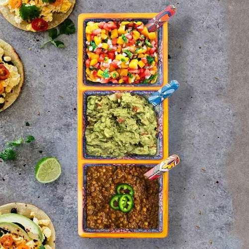 A three section tray with different types of dips such as salsa and guac on a concrete surface with tortillas and limes.