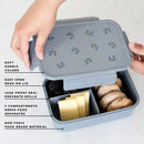Person holding the lid of a gray bento box with blue floral pattern with the main bento box below filled with food and informational text listing details.