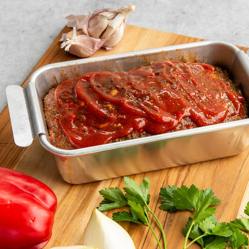 Meatloaf in a loaf pan on a wooden cutting board with vegetables.