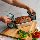 Person holding a loaf of meatloaf with oven mitts on a wooden cutting board.