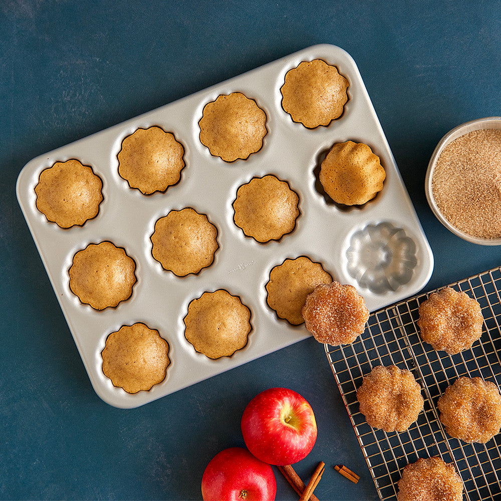 Baked apple cider treats in a mini bundt pan with apples and cinnamon on a blue background