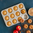 Baked apple cider treats in a mini bundt pan with apples and cinnamon on a blue background