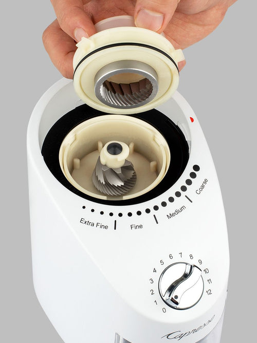 White coffee grinder with adjustable settings being held by a hand on a gray background