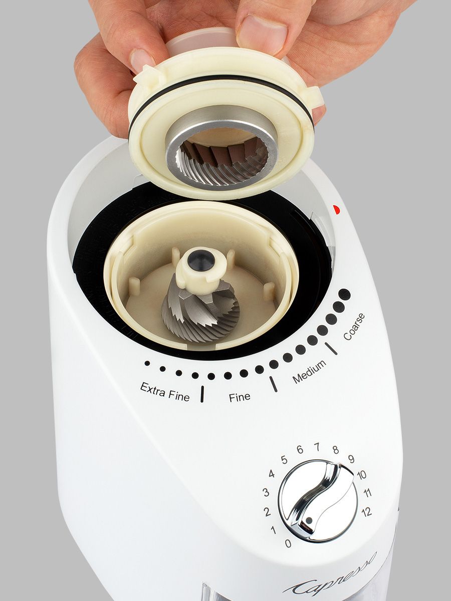 White coffee grinder with adjustable settings being held by a hand on a gray background