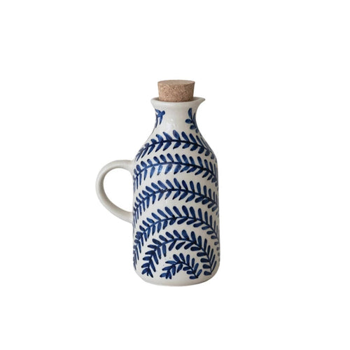 White ceramic oil bottle with blue leaf pattern and cork stopper on a white background