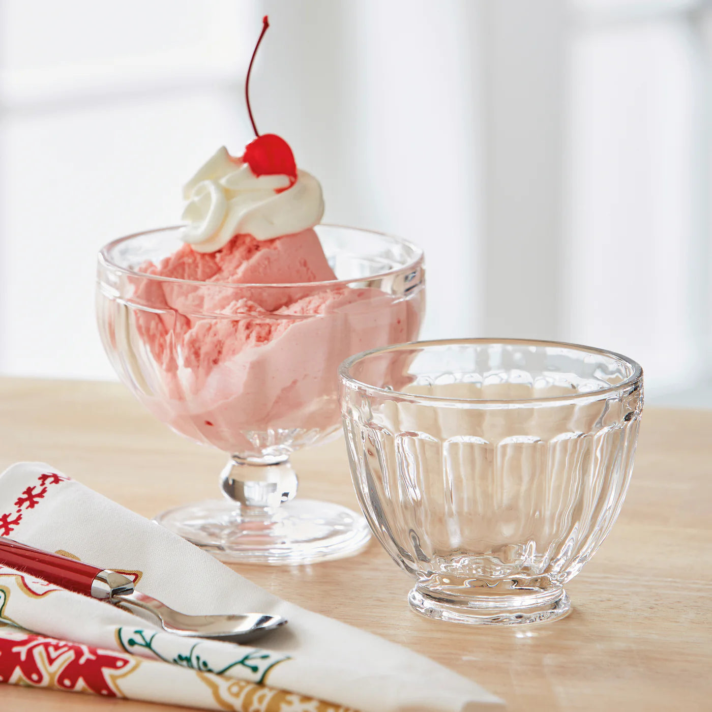 Glass bowl with pink ice cream and cherry on a wooden table