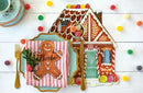 Decorative gingerbread house placemat and gingerbread man cookie table accent on a plate with colorful candies on a white wooden surface.