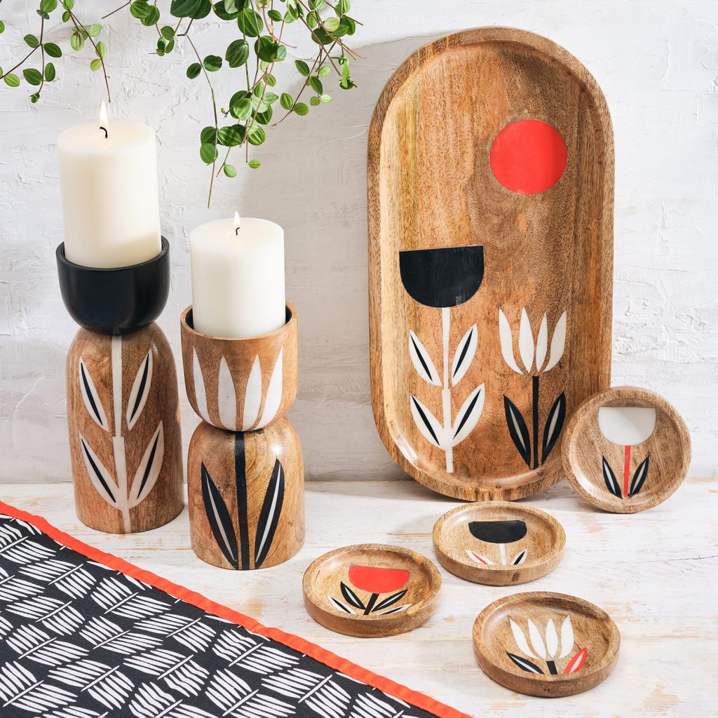 A table featuring a table runner, candle holders, plate, and coasters with simple black, white, and tangerine floral designs.