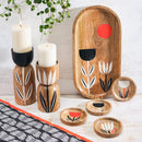 A table featuring a table runner, candle holders, plate, and coasters with simple black, white, and tangerine floral designs.