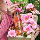 Bottle of A&Z Oregon Rosé Wine surrounded by pink flowers in a wooden crate.
