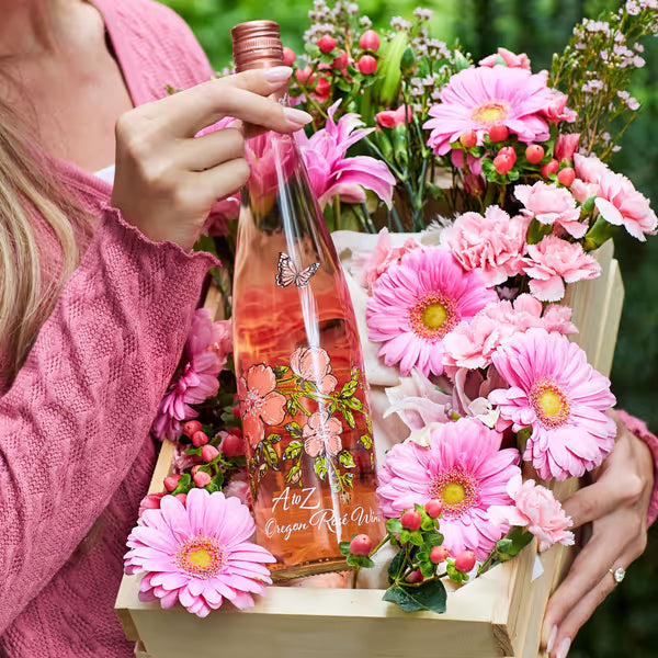 Bottle of A&Z Oregon Rosé Wine surrounded by pink flowers in a wooden crate.