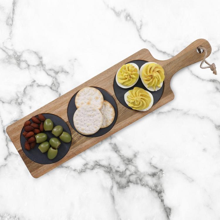 Wooden board with black slate circles holding deviled eggs, crackers, and olives on a marble background