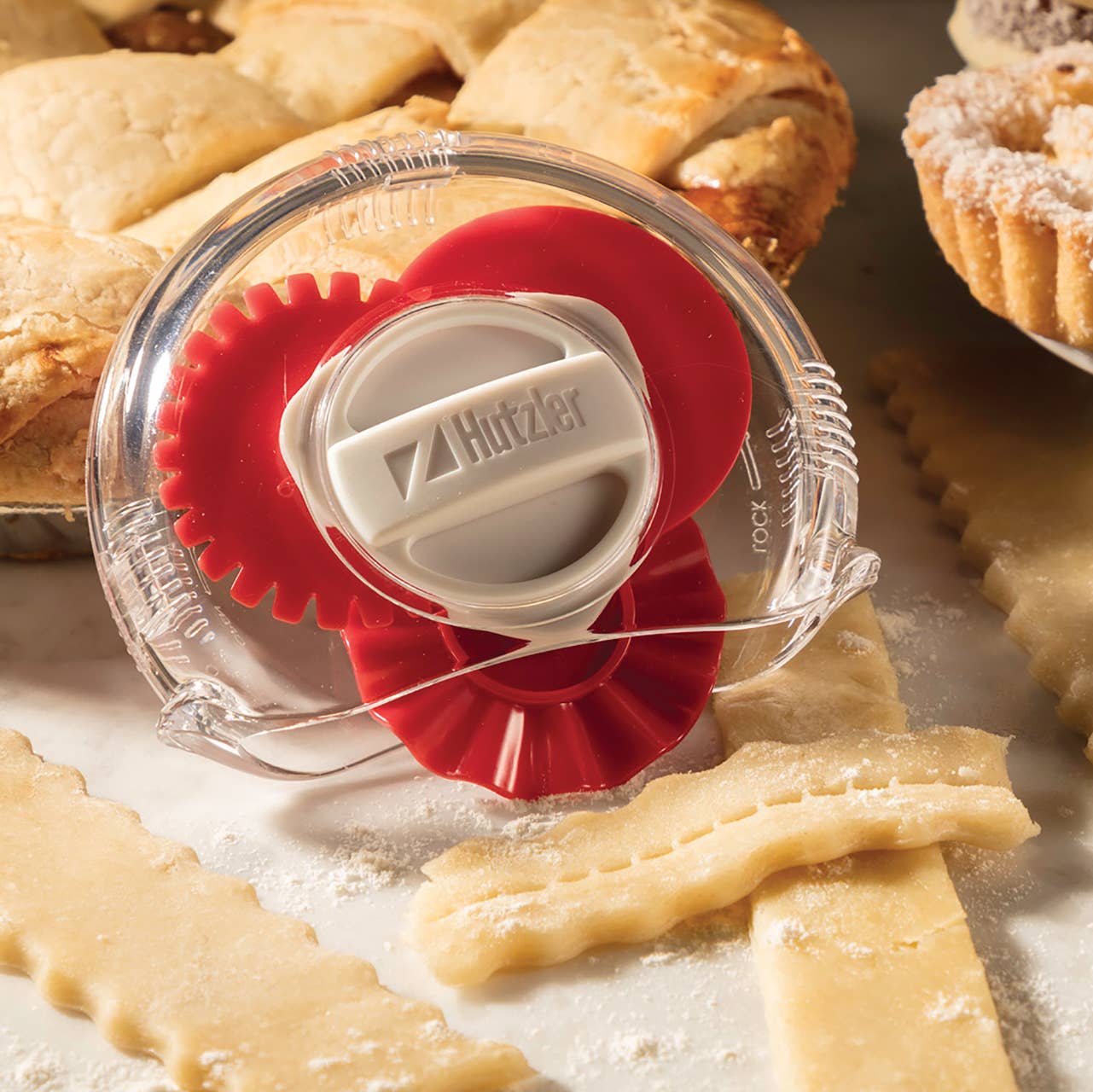 A red adjustable pastry trimmer among pieces of dough and a pie.