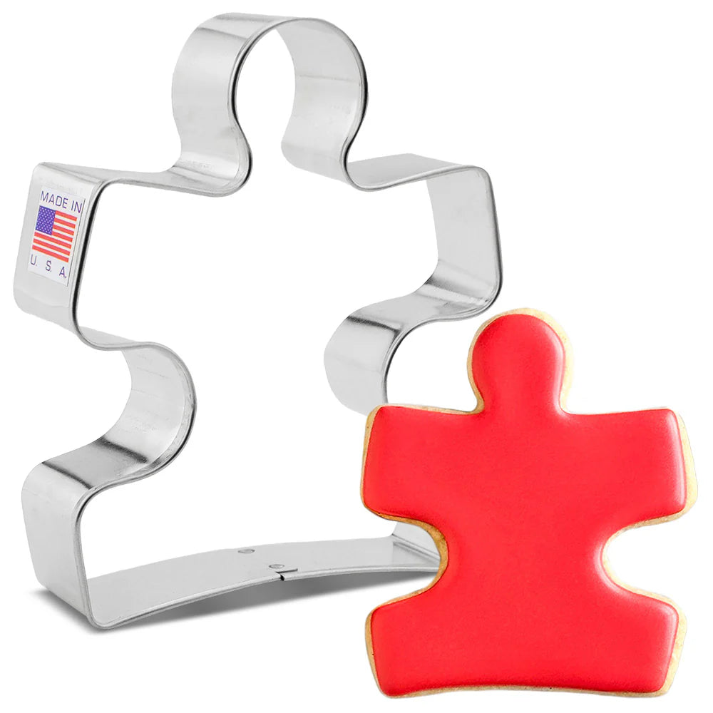 Cookie cutter shaped like a puzzle piece with a red cookie on a white background