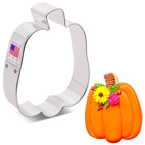 A metal pumpkin-shaped cookie cutter next to a decorative orange pumpkin cookie with flowers on top.