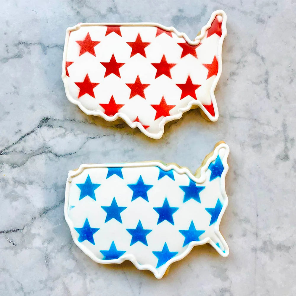 Two cookies shaped like the United States with red and blue stars on a marble surface