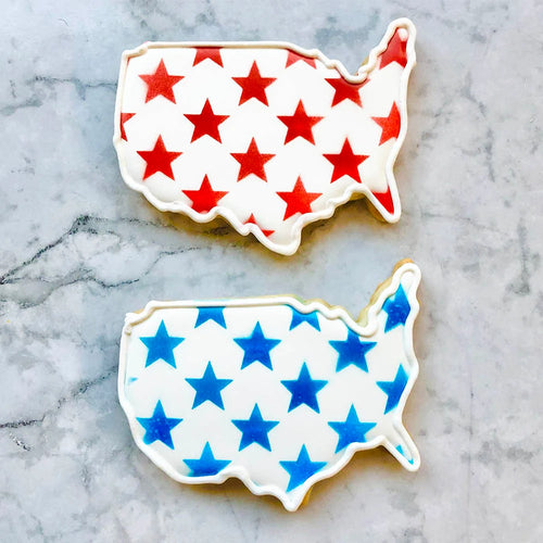 Two cookies shaped like the United States with red and blue stars on a marble surface