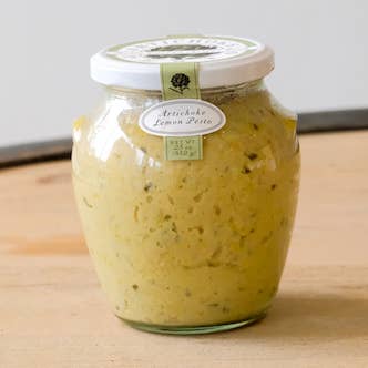 Jar of lemon artichoke sauce on a wooden surface with a neutral background