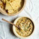 Bowl of dip with a wooden spoon and tortilla chips on a light background