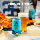 Athletic Brewing Co. can and glass of beer on a table with food in the background