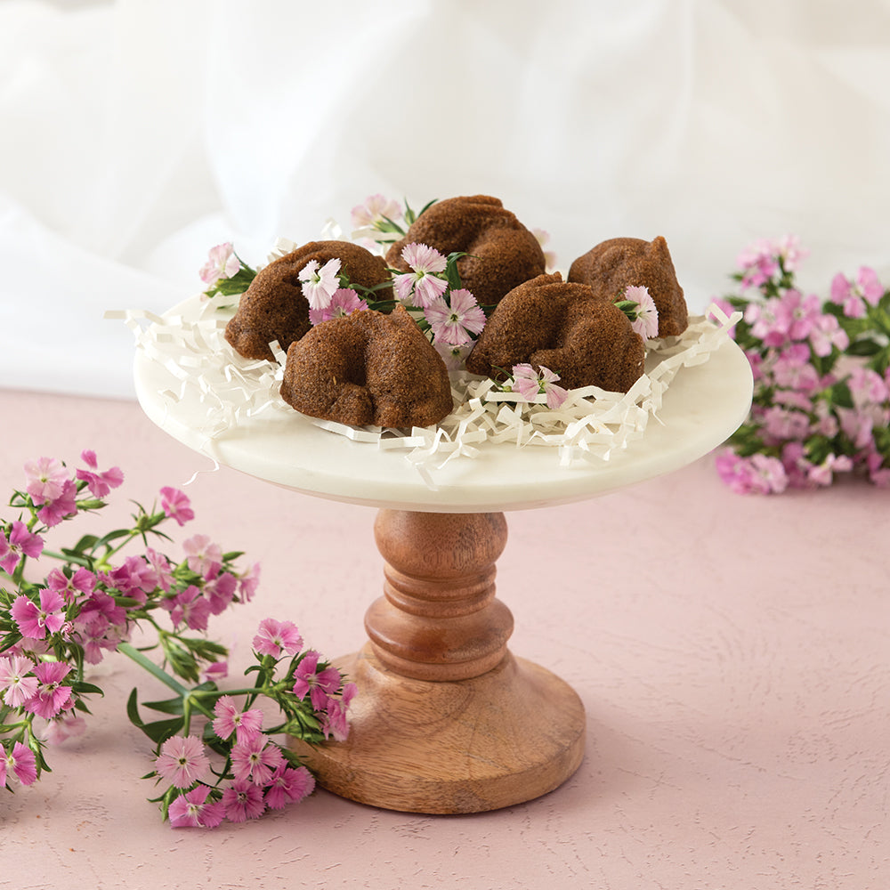 Decorative display of small brown bunny cakes on a white pedestal with pink flowers on a light pink background