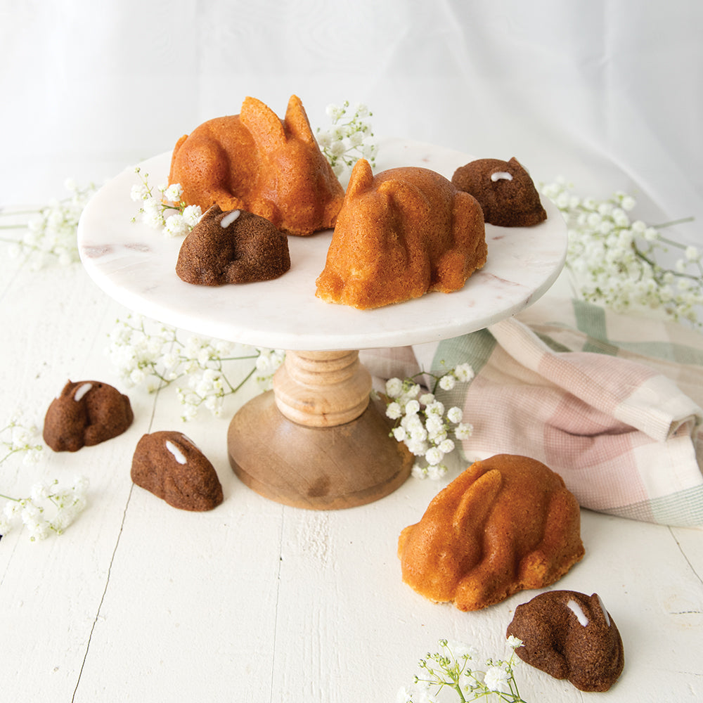 Small bundt cakes shaped like bunnies on a white stand with white flowers around.