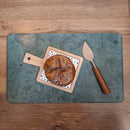 Round bread on a wooden cutting board with a cheese knife on a green marble cutting board.