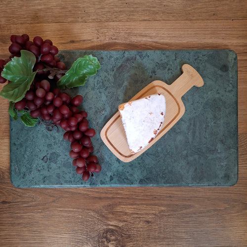 Sliced white cheese on a wooden board with red grapes on a green marble surface, all on a wooden table.