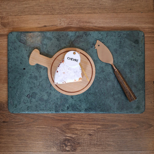 Chevre cheese on a wooden board with a cheese knife on a green marble surface, all on a wooden table.
