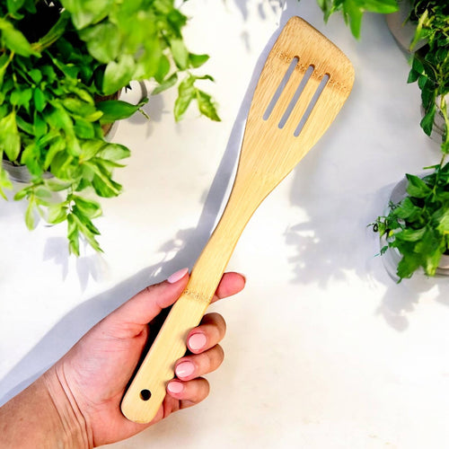 Hand holding a wooden spatula with plants in the background
