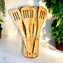 Set of wooden spatulas in a glass container with plants in the background