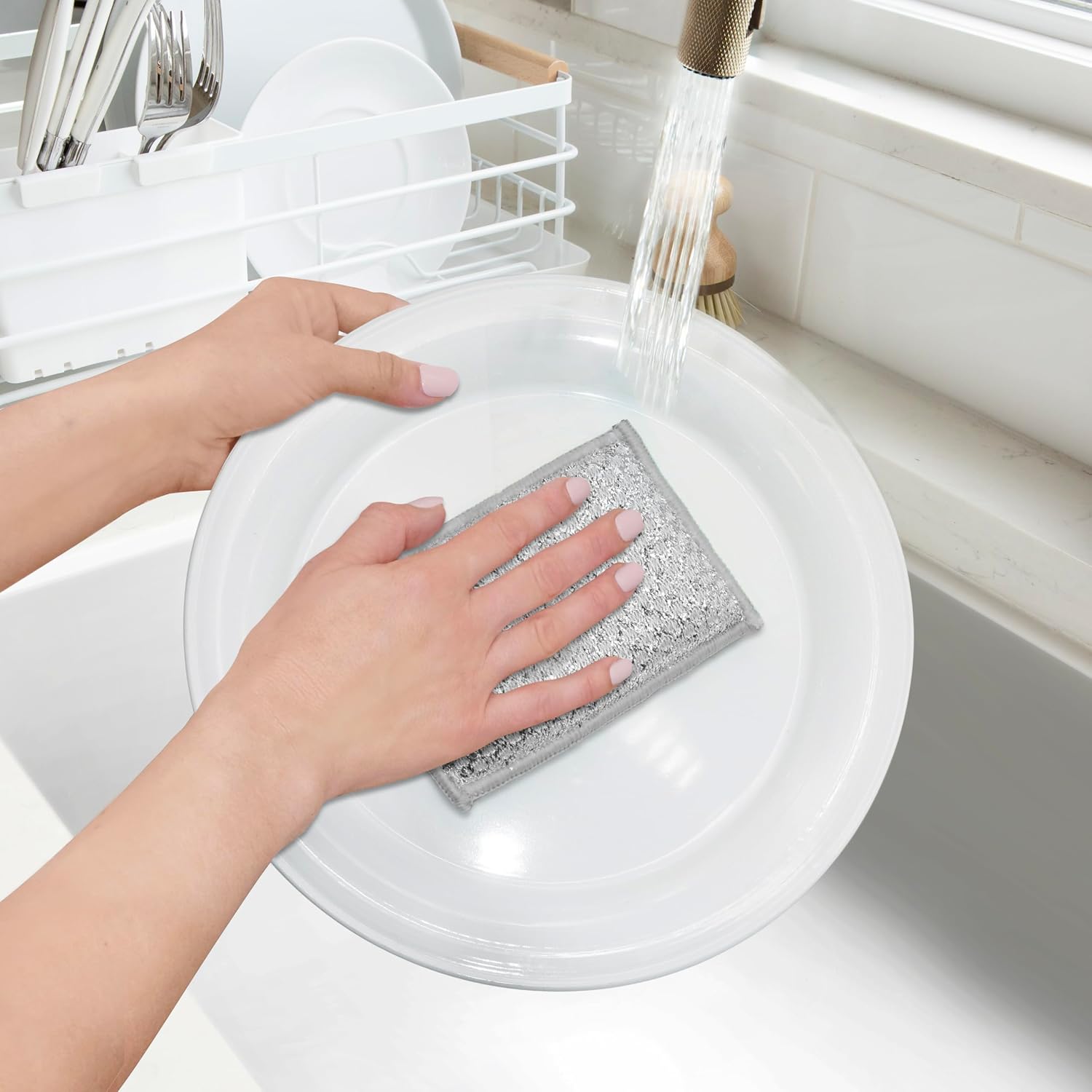 Person cleaning a white plate with a silver scrubber in a kitchen.