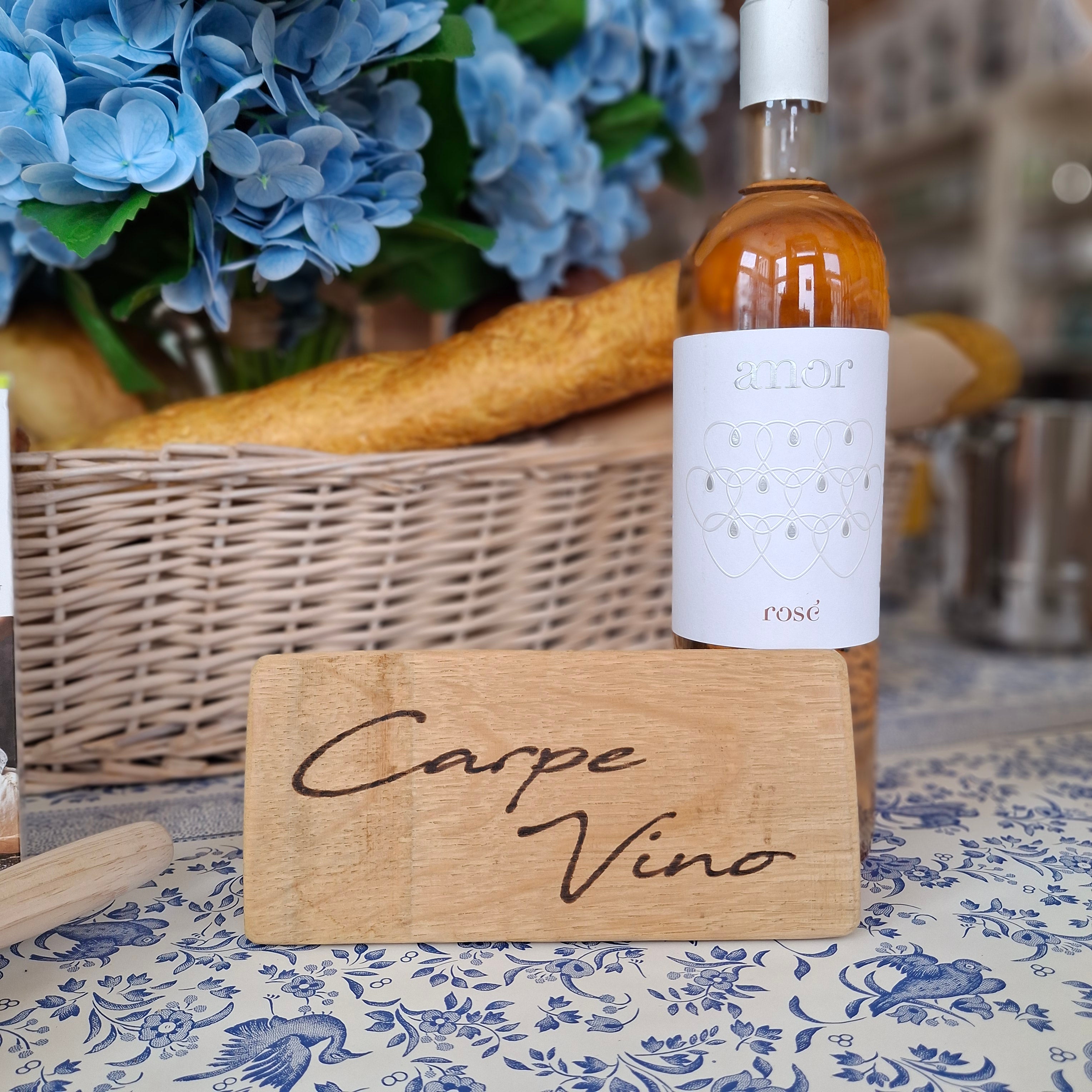 Wine bottle with a wooden holder labeled 'Carpe Vino' on a decorative surface with blue flowers.