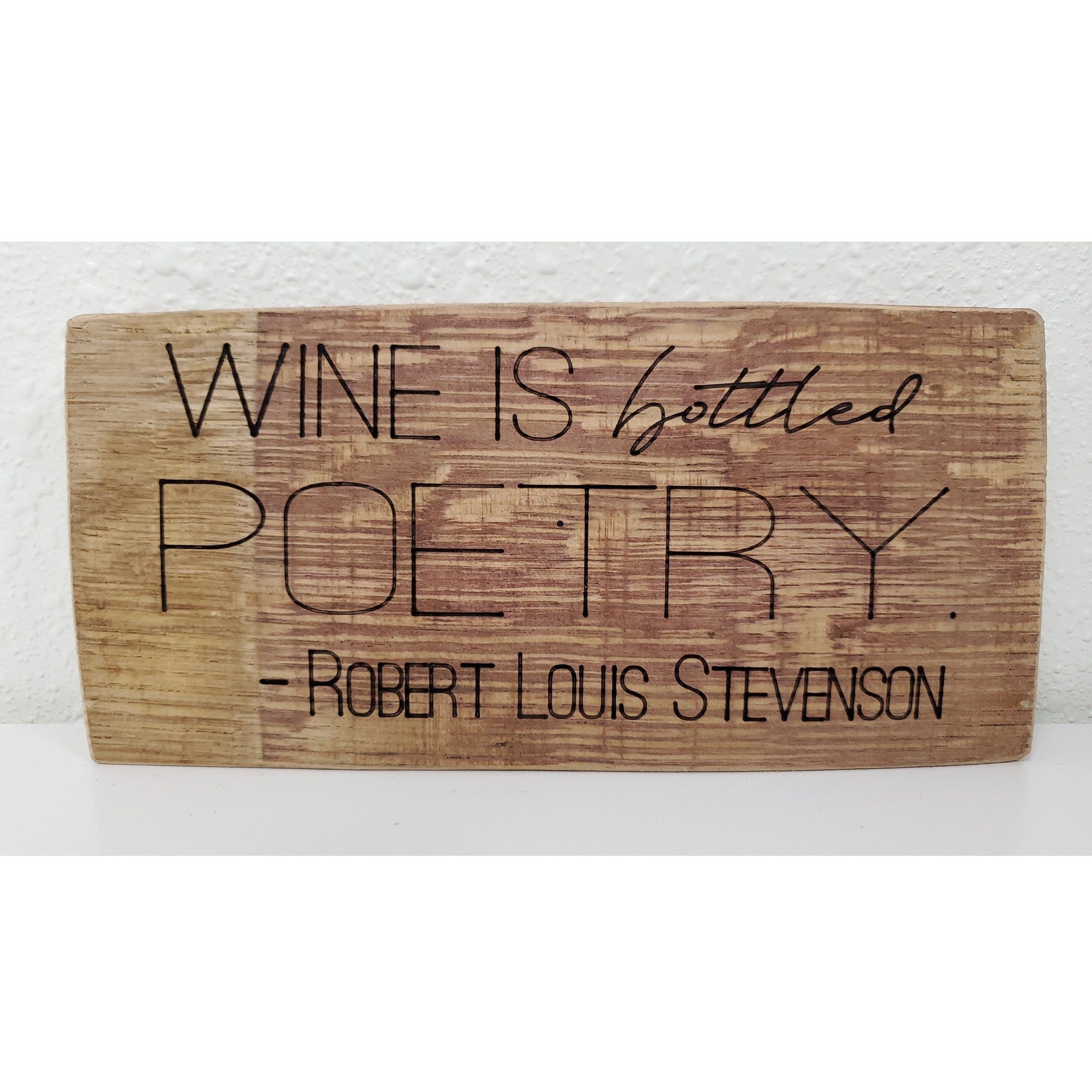 Wooden sign with engraved text 'Wine is bottled poetry. Robert Louis Stevenson' on a white background