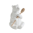 White ceramic bear-shaped honey container with a wooden dipper on a white background