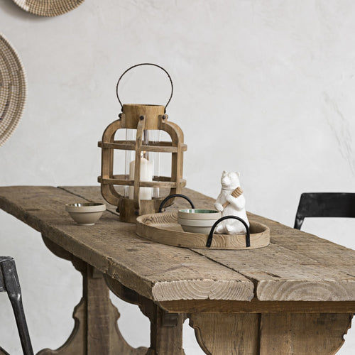 Wooden table with decorative items including a lantern and white ceramic bear honey pot with a honey dipper against a neutral background