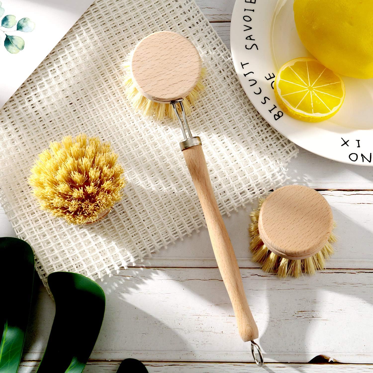 A beechwood cleaning brush with additional brushes and a plate with citrus slices on a mesh mat and wood table.
