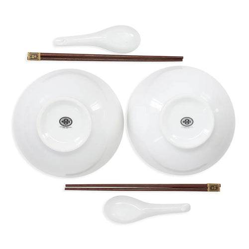 A white ceramic dinnerware set featuring two bowls shown from the bottom, two dark brown chopsticks with gold-toned ends, and two white spoons, arranged symmetrically on a white background.