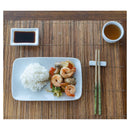 A bamboo placemat with a drink, soy dish, plate of food, and chopsticks on a chopstick rest.