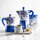 Blue and white ceramic espresso pots next to cups of espresso and food on a light background