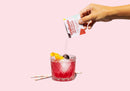 Hand pouring a Craftmix drink mix into a glass with a pink background