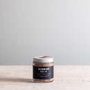 A jar of Jacobsen Salt Co. Black Garlic Salt infused sea salt, placed on a light surface.