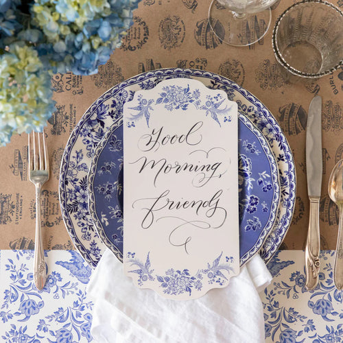 Decorative table setting with blue and white floral plates, silverware, and a card with 'Good Morning, Friend' text.